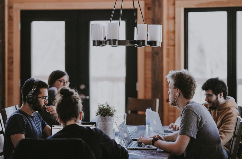 des personnes dans une salle, autour d'une table avec des ordinateurs, en train de discuter